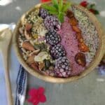 סמודי בול ללא סוכר וגלוטן מוגש בתוך קערת עץ בהירה עם שורות של תוספות, פטל, נענע, ג׳וגי, צ׳יה. עלי נענע לקישוט