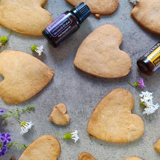 עוגיות לבנדר בצורת לב מונחות על נייר אפייה ולידם תמצית לבנדר בתוך כלי קטן, פרחים קטנים לבנים לקישוט