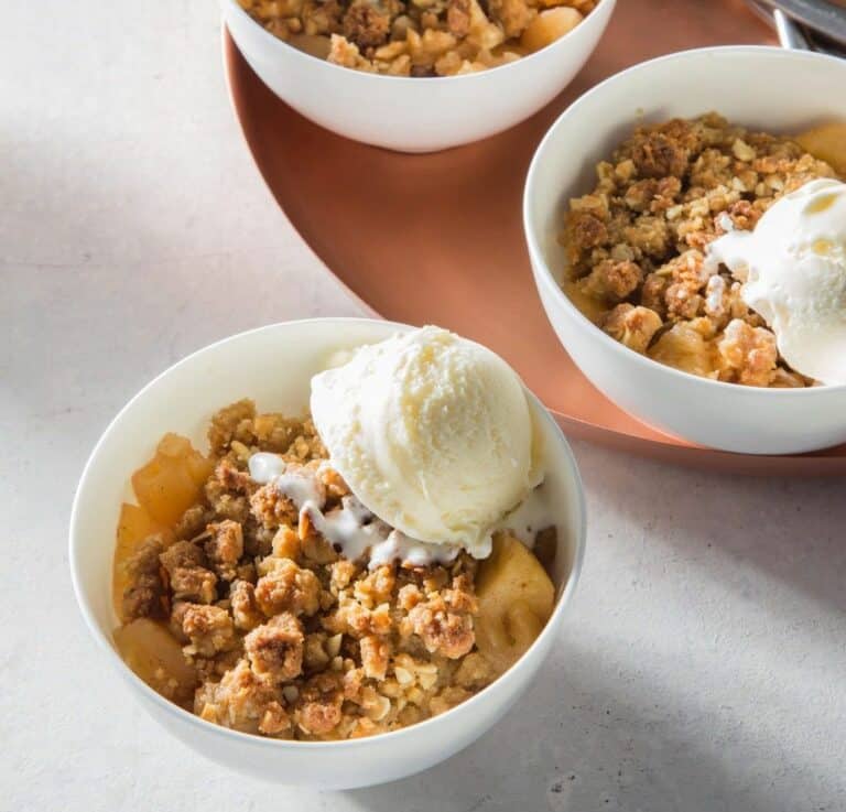 קרמבל תפוחים בתוך קערה לבנה עם סקוף של גלידה וניל בצד