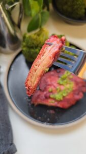 פטריית רעמת האריה ברוטב אדום מונח על צלחת שחורה עם שוליים בהירים וירקות ירוקים בצד