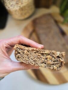 דייסה אפויה בצורת עוגה, עם זרעי צ׳יה, פרוסה מוחזקת בין שתי אצבעות וברקע שאר העוגה מונחת על צלחת עץ