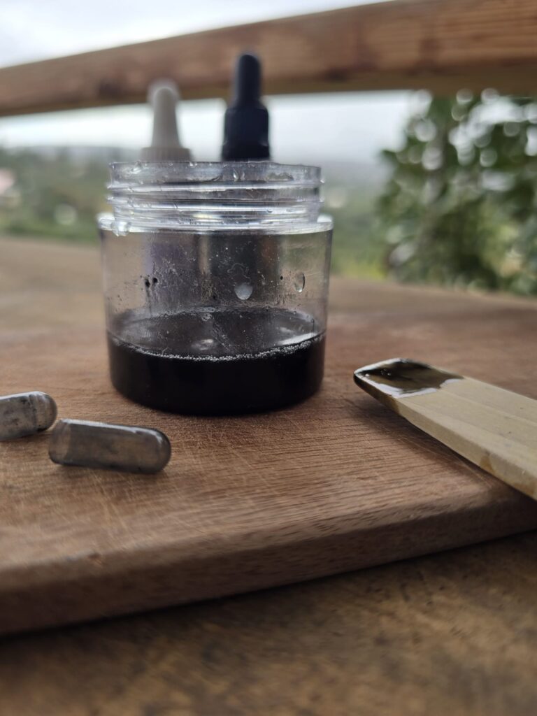 משחה לפטרייה בנרתיק בצבע שחור בתוך צנצנת זכוכית מונחת על מגש עץ על רקע ירוק של עצים